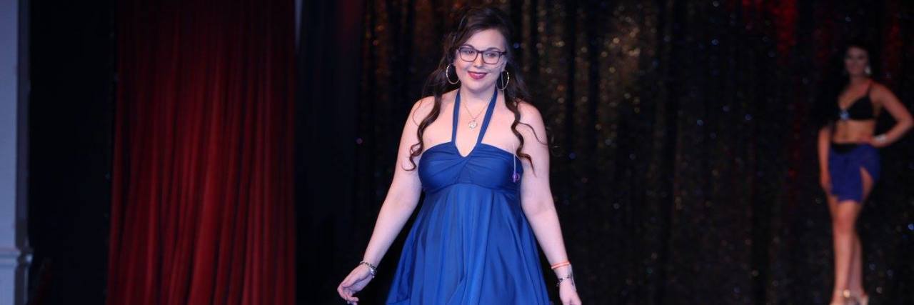 A photo of the writer walking down the runway in a beautiful knee-length blue dress.