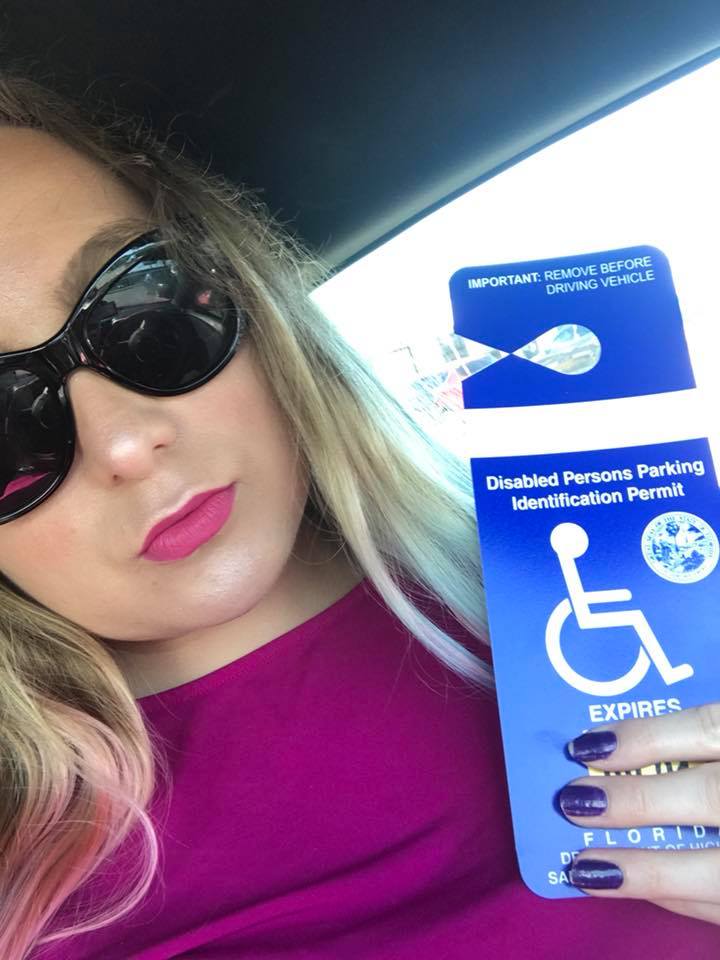 woman wearing a pink shirt and sunglasses holding her disability parking pass