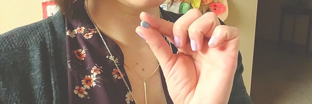 Blogger Shares Selfie With Antidepressants Woman holding a small blue pill. She has short brown hair.