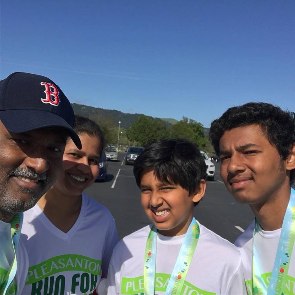 woman with her husband and two sons standing outside in front of a lake wearing matching t-shirts and medals