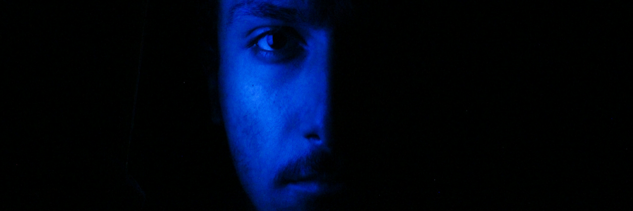 half of mans face with black background and he is blue