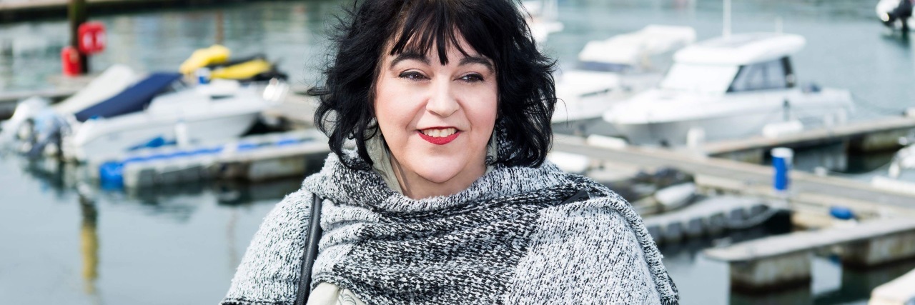 Constantly Going Through the Grieving Process With Fibromyalgia woman wearing a black and white shawl and standing in front of a dock with boats