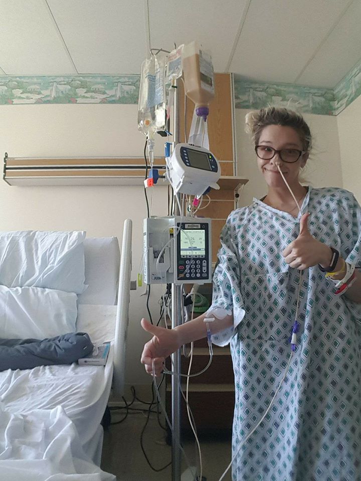 woman wearing a hospital gown and standing next to an IV pole with a tube in her nose