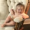 Baby with Down syndrome sitting on white rocking chair smiling at camera