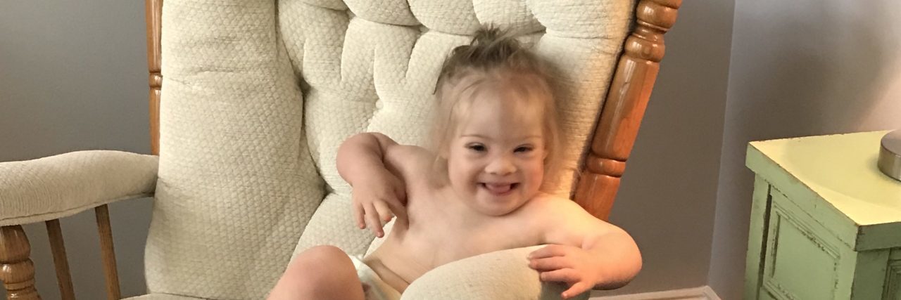 My Daughter With Down Syndrome Is as Loved as Her Siblings Baby with Down syndrome sitting on white rocking chair smiling at camera