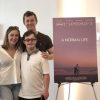 Alex with his brother and mom standing next to movie poster for "A Normal Life."