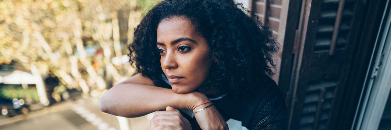 17 Comments People With Depression Dread Hearing Black woman sitting on a terrace resting her head on her arm with neutral expression