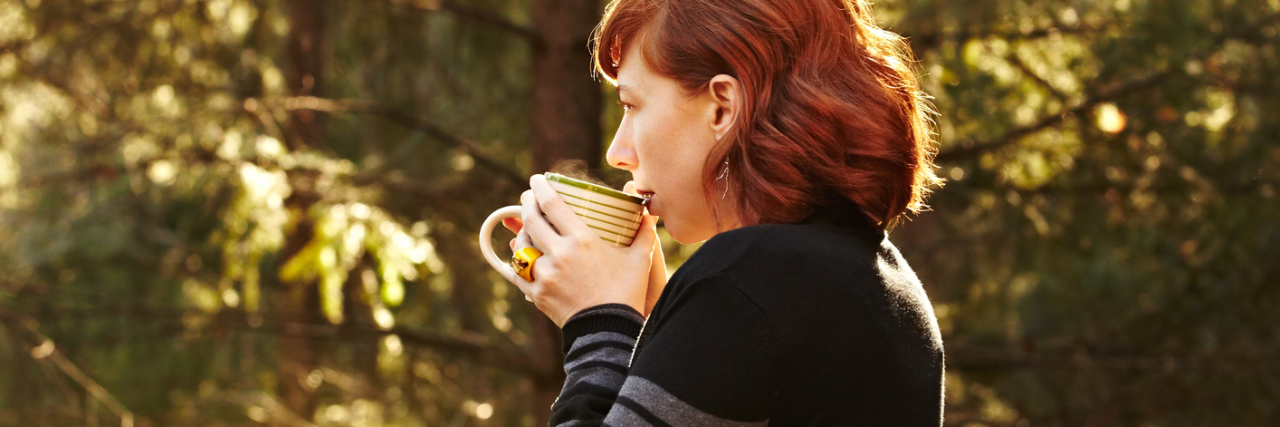 woman standing outside on her porch drinking coffee surrounded by trees