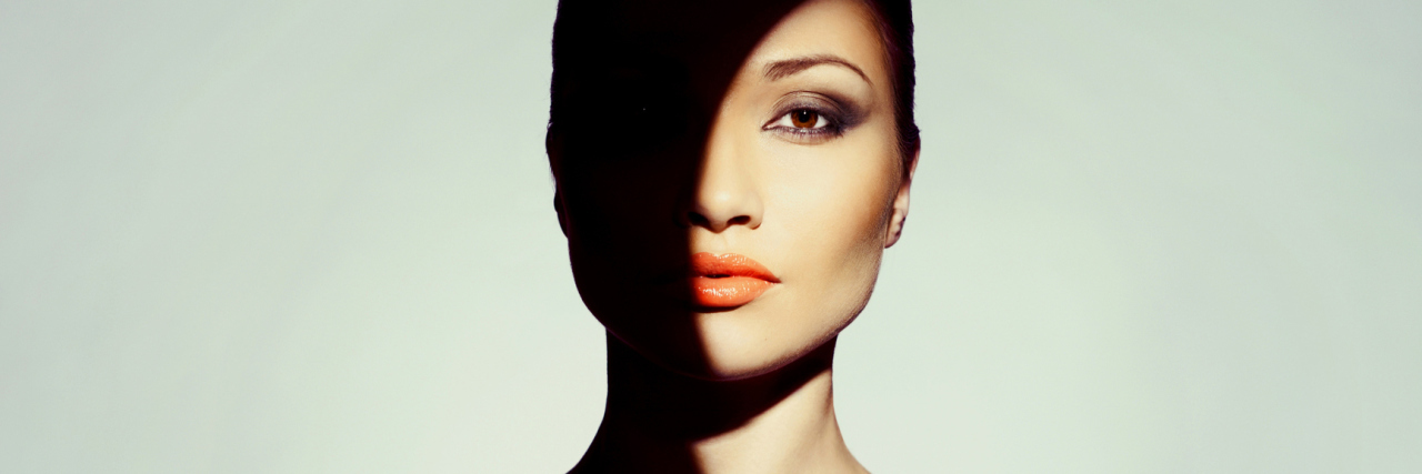 The Visible Symptoms of My 'Invisible' Illness woman covered mostly in shadow with a partial circle of light illuminating part of her face and shoulder