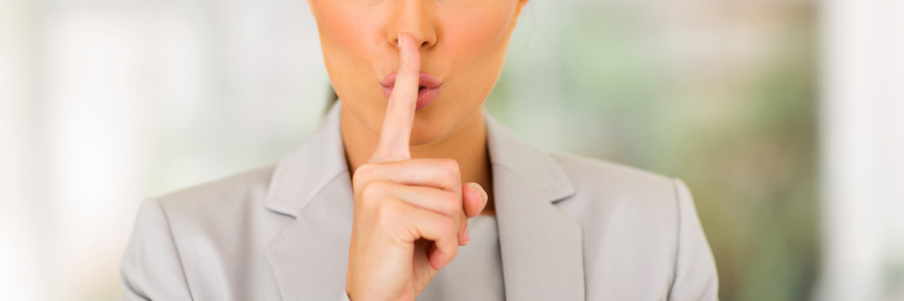 The Reality of What It's Like to Work With Chronic Illness businesswoman in a gray suit saying shh