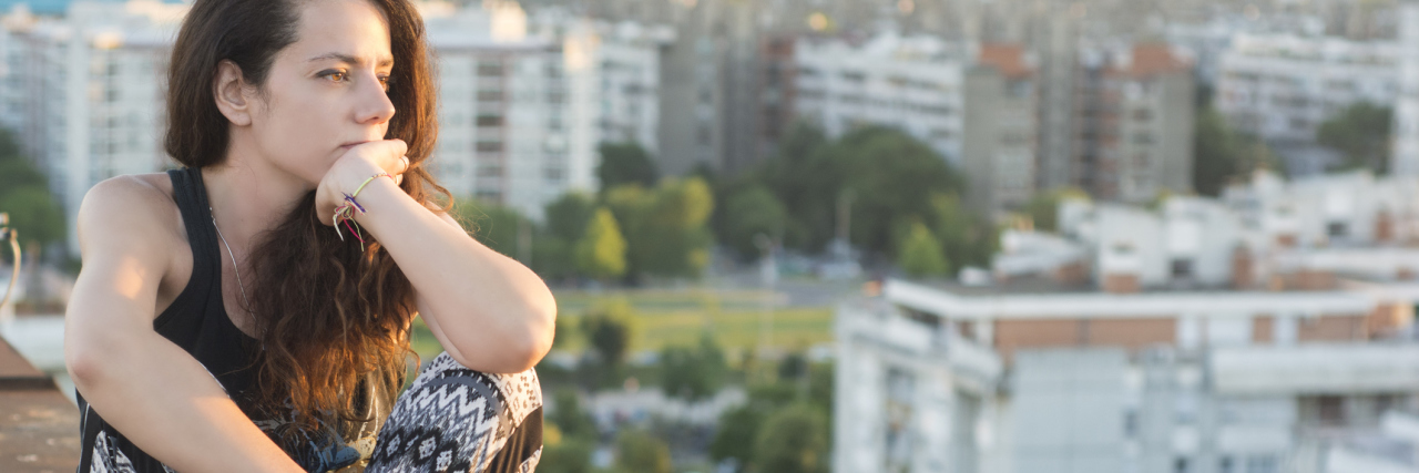 What It's Like to Have Fibromyalgia in Your 20s woman sitting on the ledge of a building and looking out at a city