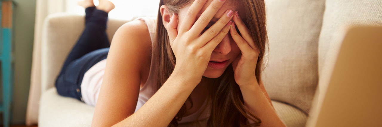 Tips for Managing Health Anxiety You Can Use Right Now young woman lying on couch in front of laptop looking concerned and anxious