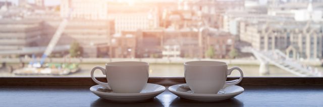Two cups of coffee with panoramic view of a city in background.
