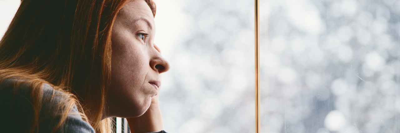 Adopting a Better Mindset About Living With Chronic Illness woman looking out the window at a snowy landscape
