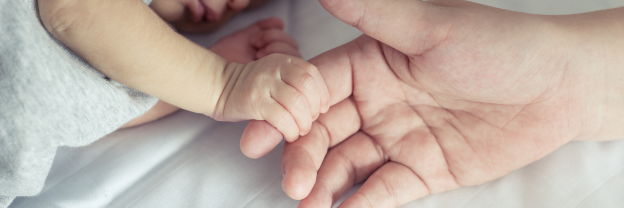mother's hand holding her newborn baby's hand