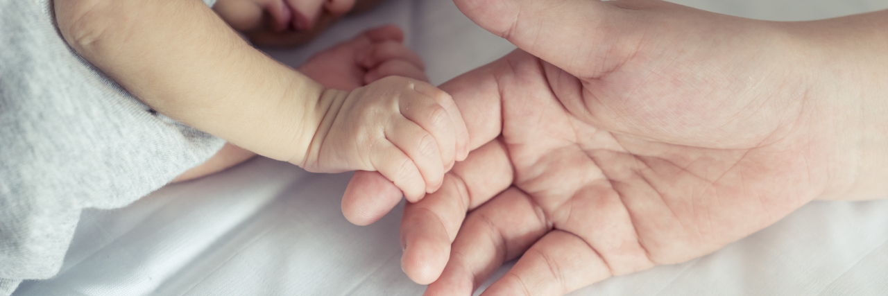 The Hardest Parts of Parenting a Child With a Rare Condition mother's hand holding her newborn baby's hand