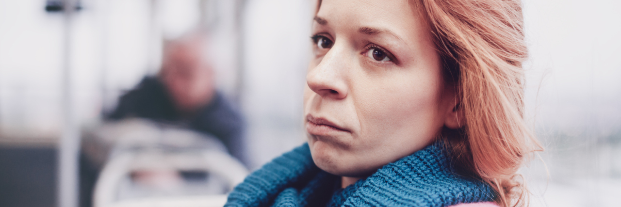 woman sitting on a bus wearing a blue scarf and looking sad