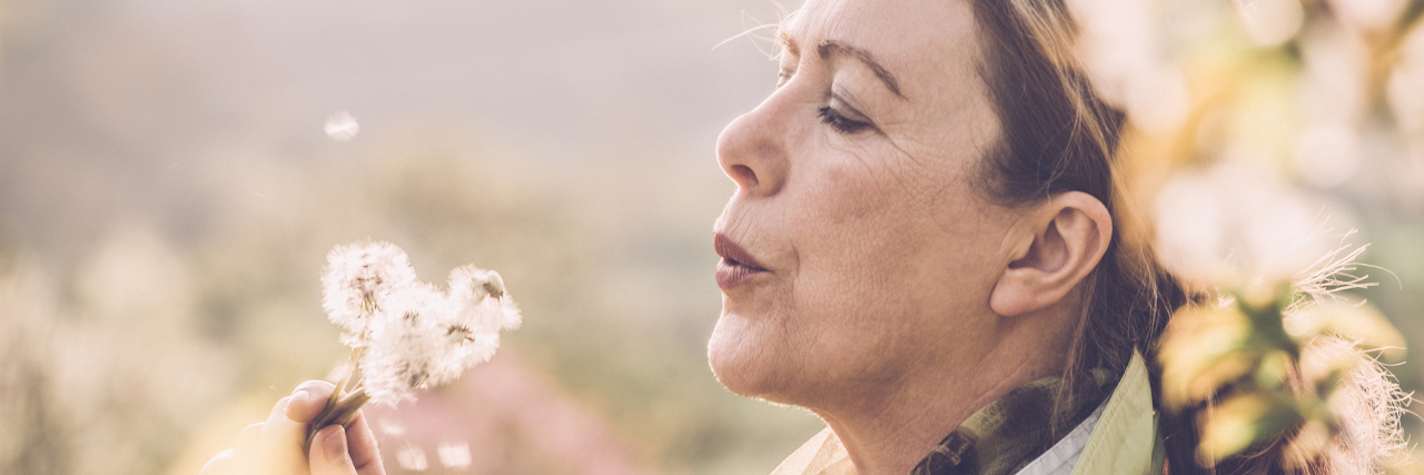 A picture of a middle-aged woman blowing on a dandelion.