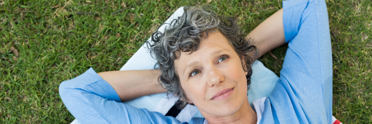 4 Ways I Manage the Emotional Stress That Comes With Chronic Illness An older woman laying in the grass looking peaceful.