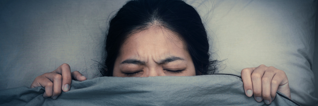 What People With Chronic Illness Dream About at Night woman lying in bed pulling the covers up over her head