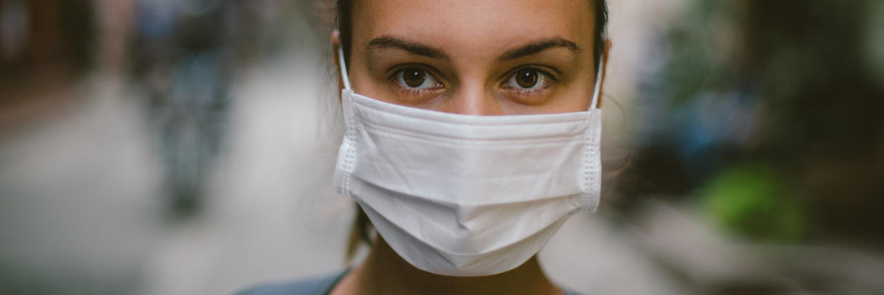 Why Germs Can Be Dangerous for People With Chronic Illness woman walking on the street wearing a face mask