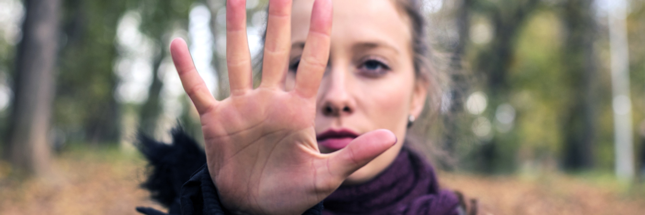 Why I'm Stopping My Habit of 'People Pleasing' Woman in woods holding hand out in stop gesture
