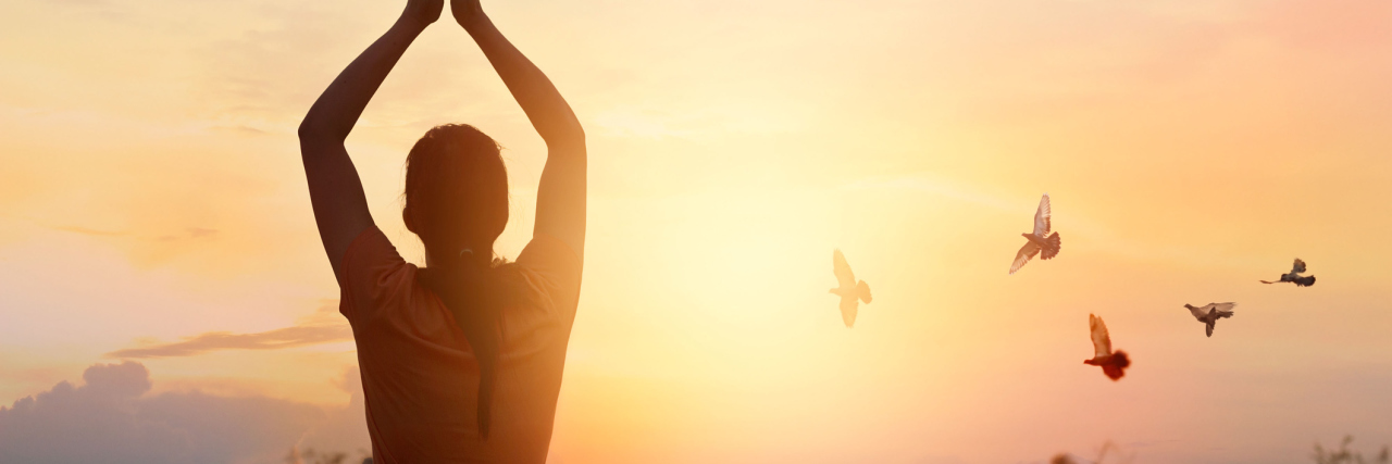 woman praying outside at sunset with birds flying overhead