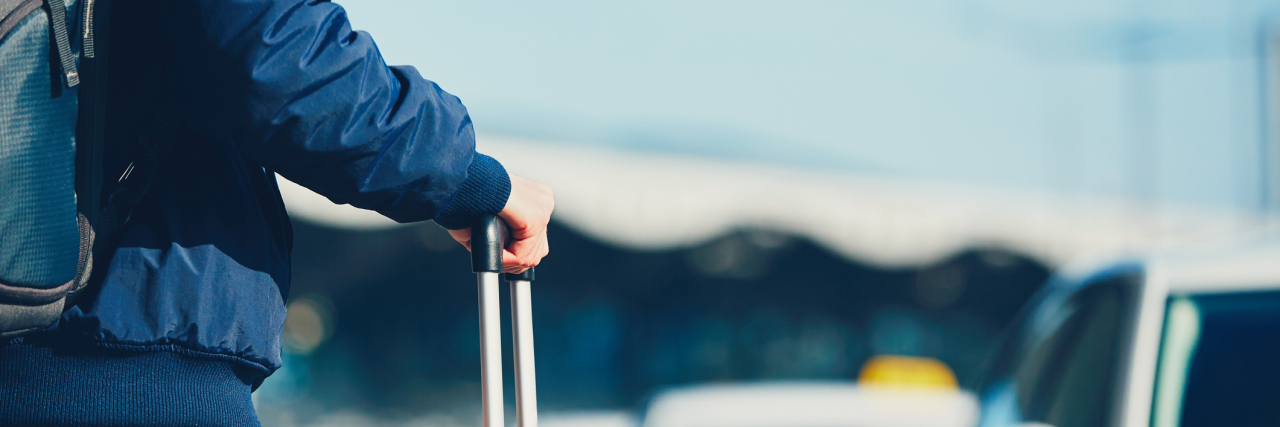 What I Learned From Going on Vacation With Chronic Illness man standing with his suitcase waiting for a taxi