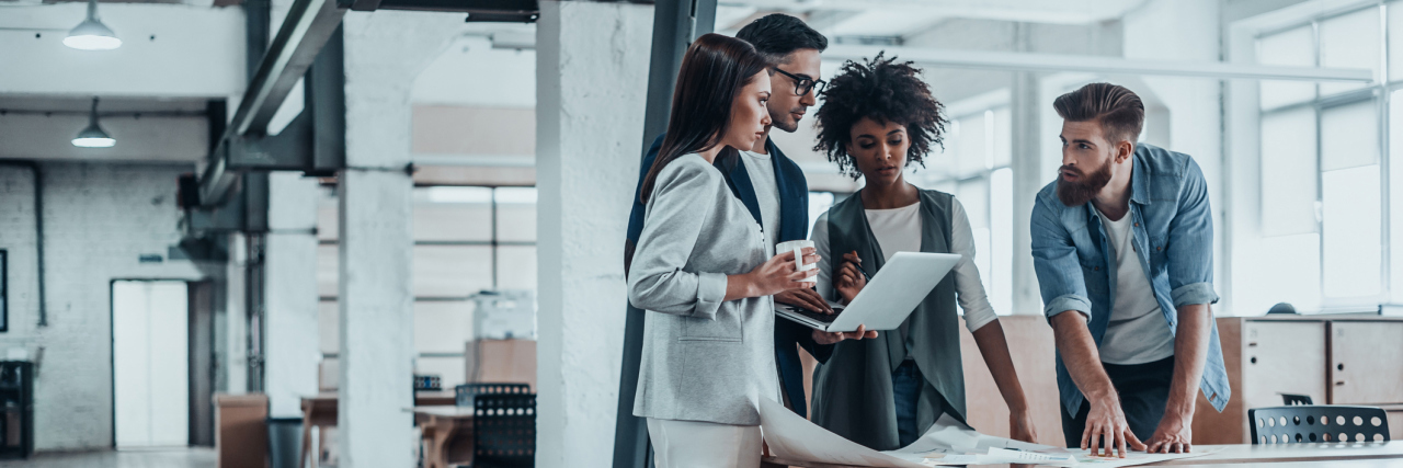 Deciding When to Tell Coworkers About Your Illness group of coworkers standing over a table and talking