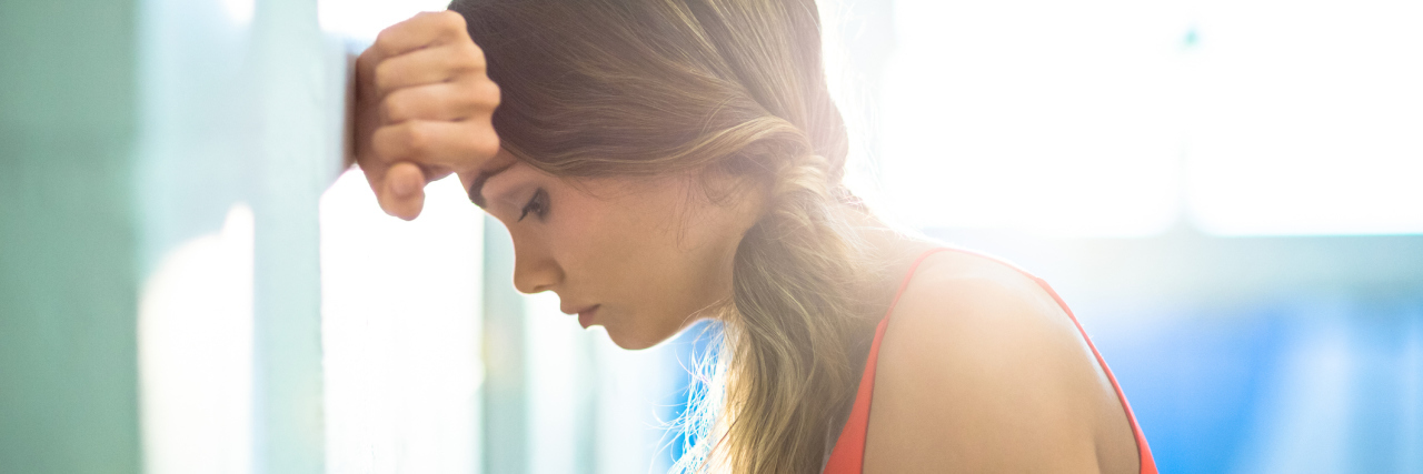 The Difficulties of Living With Brain Fog When You Have Fibromyalgia woman leaning her head against the wall