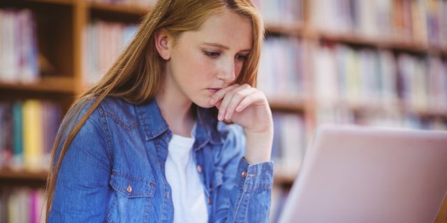 A female college student sitting in a library, while using her computer.