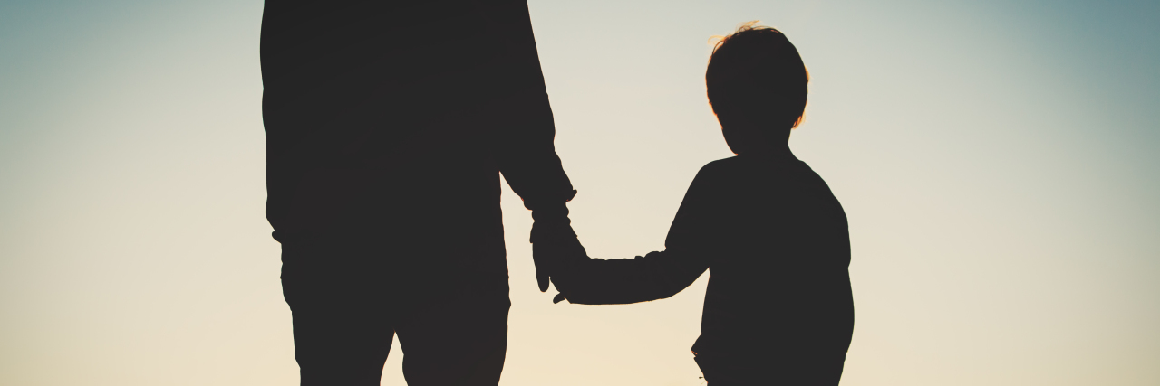 silhouette of father and son holding hands at sunset sky