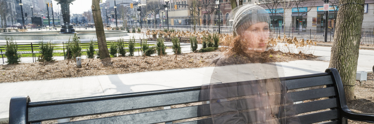 Facing Judgment When You Have an Invisible Illness blurred image of a woman sitting on a bench outside in a city