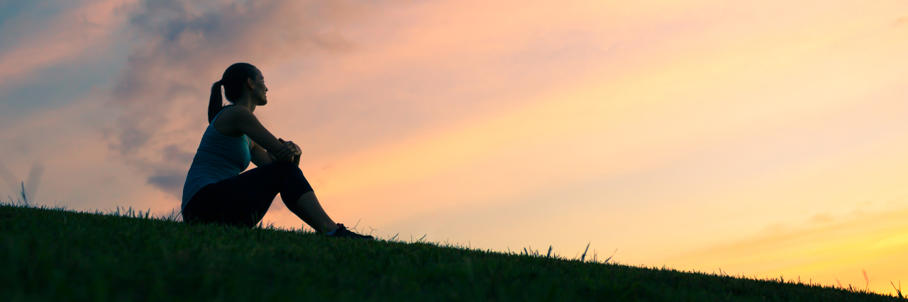 Caring for Your Parent With a Terminal Illness Young woman sitting outdoors watching sunset.