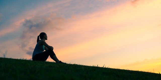 Young woman sitting outdoors watching sunset.