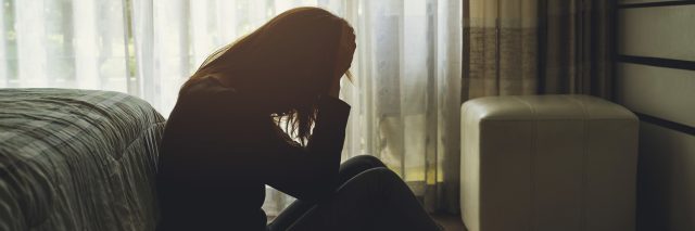 depressed woman sitting head in hands in the dark bedroom