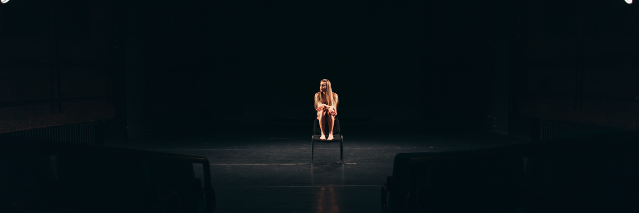 The Time for Hiding Disability Is Over Actress alone on stage sitting barefoot on a chair.