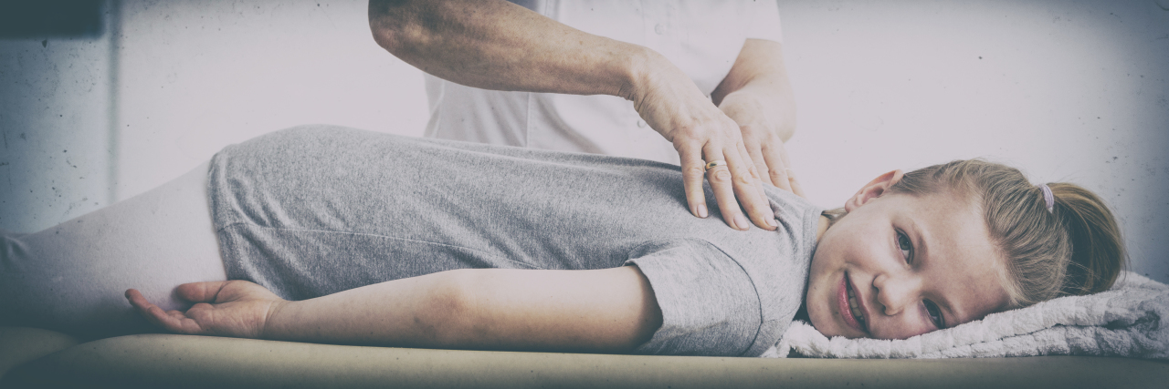 Psychological Effects of Childhood Scoliosis Girl lying on physiotherapy table getting spine examined.