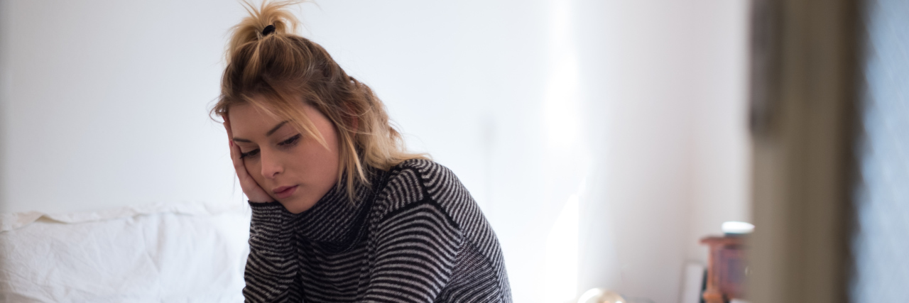 The Judgment That Comes With Going on Disability A woman sitting on a bed, looking sad.