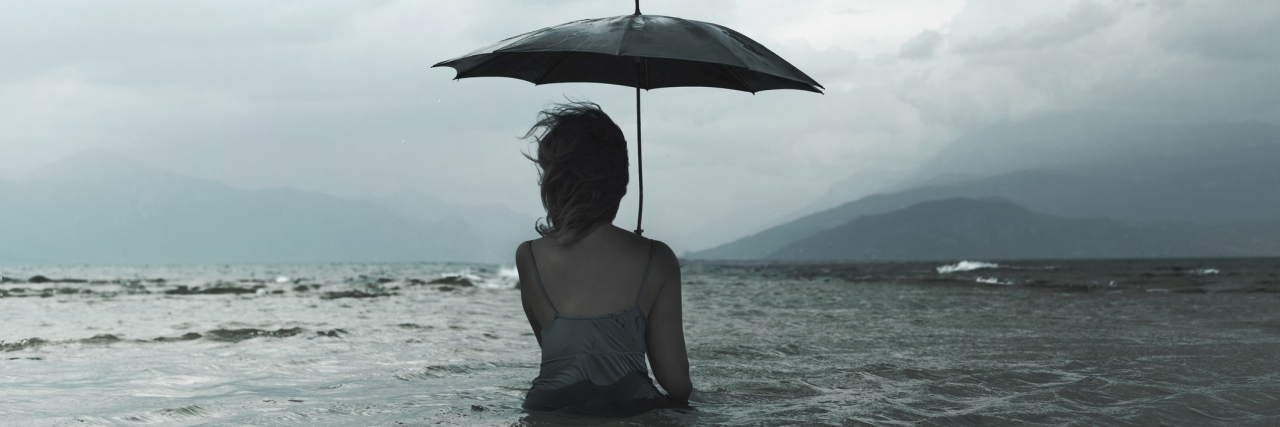A woman holding an umbrella over her head in stormy weather, while standing in the middle of a body of water that goes above her waste.