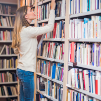 Woman standing on ladder searching for books in a library