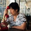 Asian women 40s white skin in black and white shirt unhappy and dismal between waiting something or talking phone call in a coffee shop cafe with a red telephone vintage style