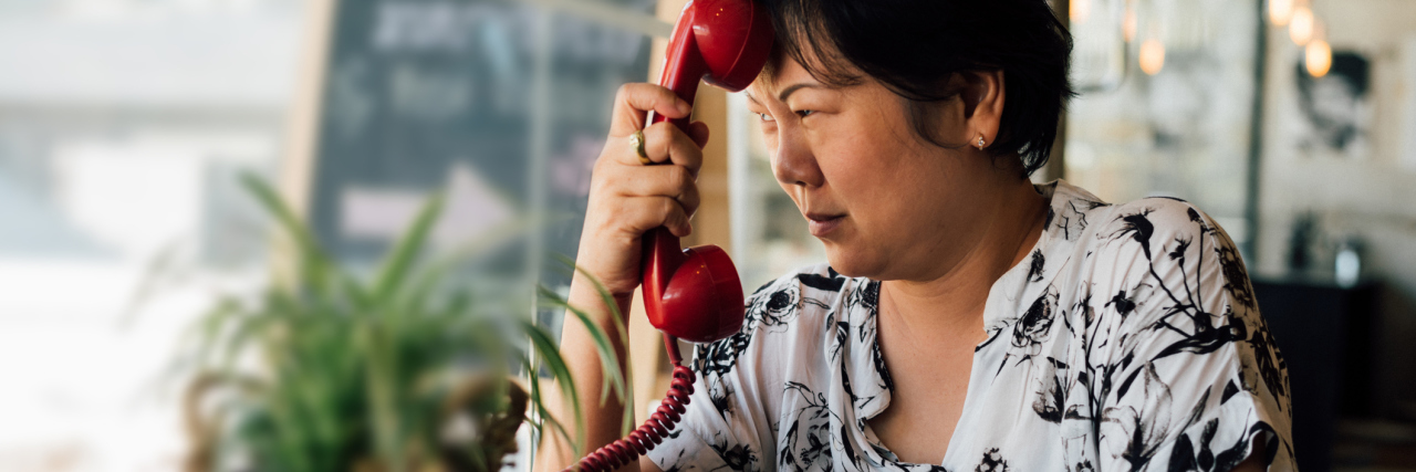 Borderline Personality Disorder and Suicidal Gestures Asian women 40s white skin in black and white shirt unhappy and dismal between waiting something or talking phone call in a coffee shop cafe with a red telephone vintage style
