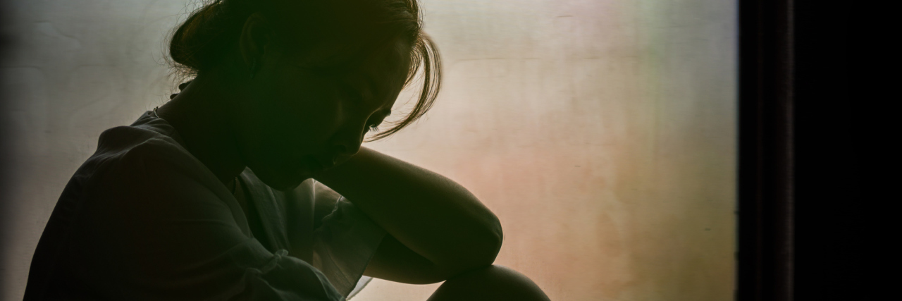 When Chronic Illness Makes You Feel Betrayed by Your Body silhouette of a woman sitting on a windowsill while it's raining