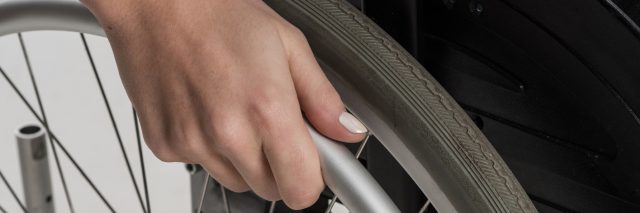A woman with painted nails with her hand on the wheel of her wheelchair.