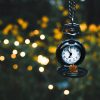 A pocket watch hanging from branches, surrounded by nature and lights in the evening light.