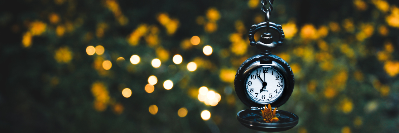 Why Endometriosis Is One Big Waiting Game A pocket watch hanging from branches, surrounded by nature and lights in the evening light.