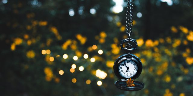 Why Endometriosis Is One Big Waiting Game A pocket watch hanging from branches, surrounded by nature and lights in the evening light.