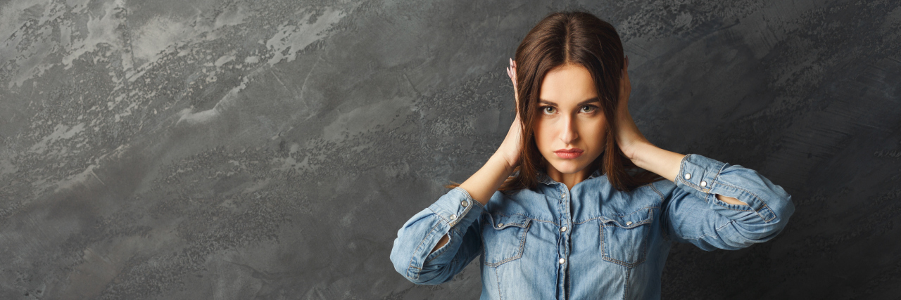 What People Really Need to Stop Saying to Those With Bipolar Disorder young woman with hands over ears against gray background