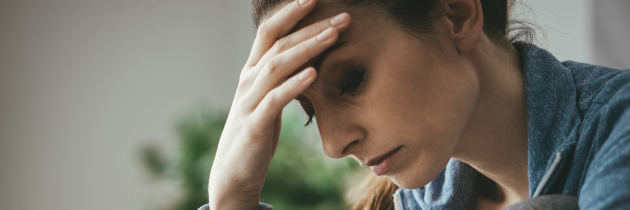 It's Time to Be Real About Myalgic Encephalomyelitis A woman looking tired, with her head in her hand.